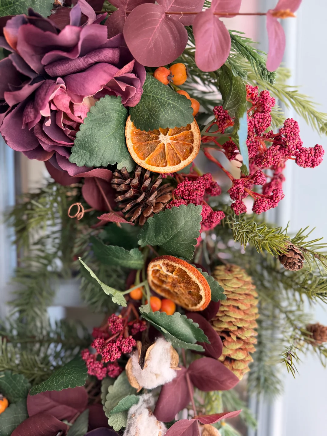 Close-up of greenery, burgundy flowers, dried orange slices, berries, pinecones, and ribbons