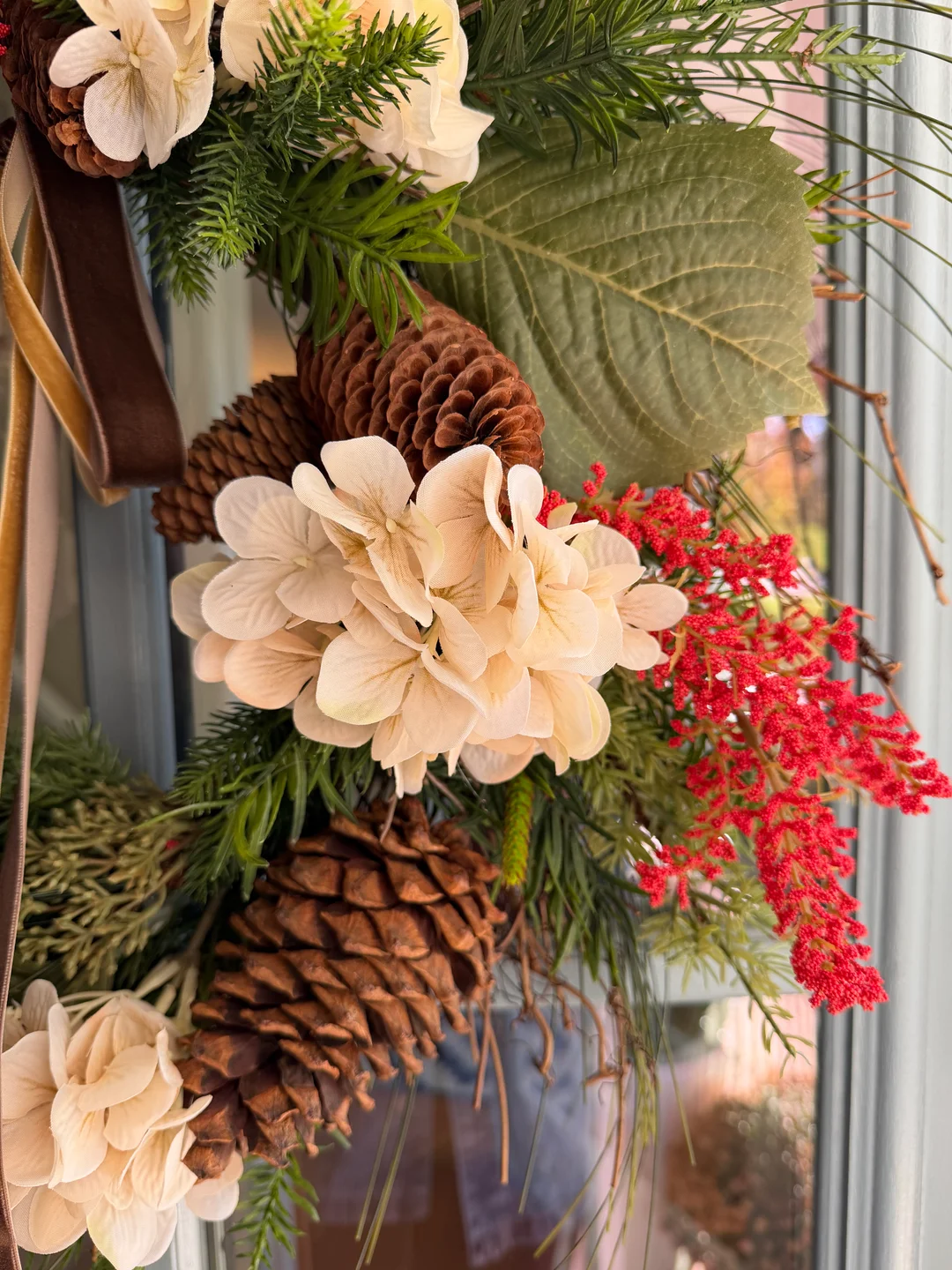 Close-up of greenery, cream flowers, red berries, pinecones, and long ribbons