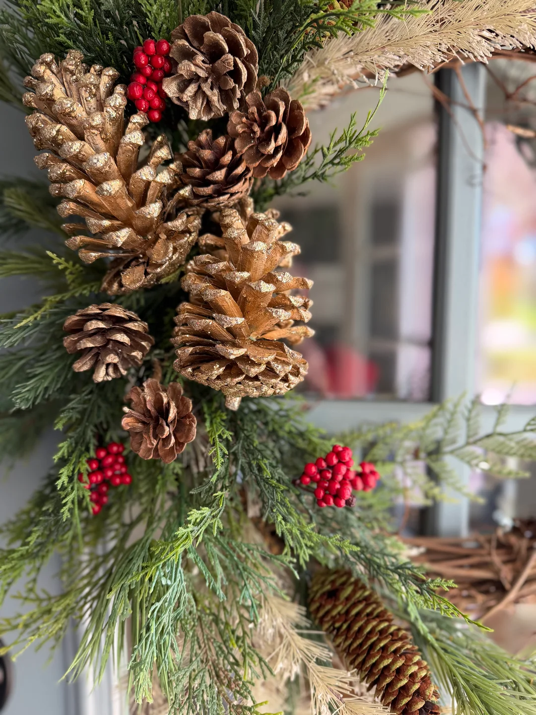 Close-up of grapevine base, greenery, pinecones, grasses, and red berries