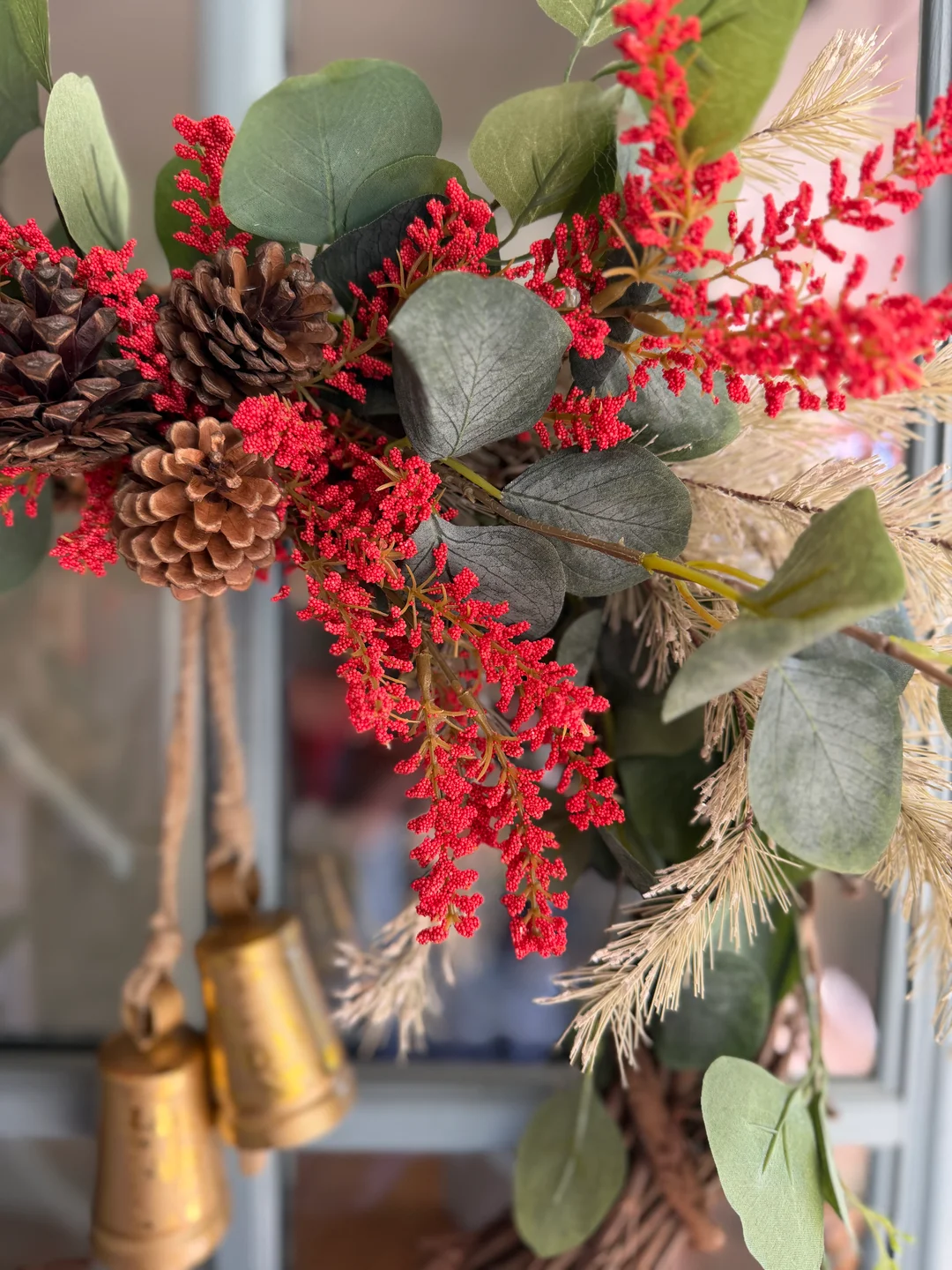 Close-up of grapevine base, greenery, red berries, pinecones, grasses, and gold-toned bells