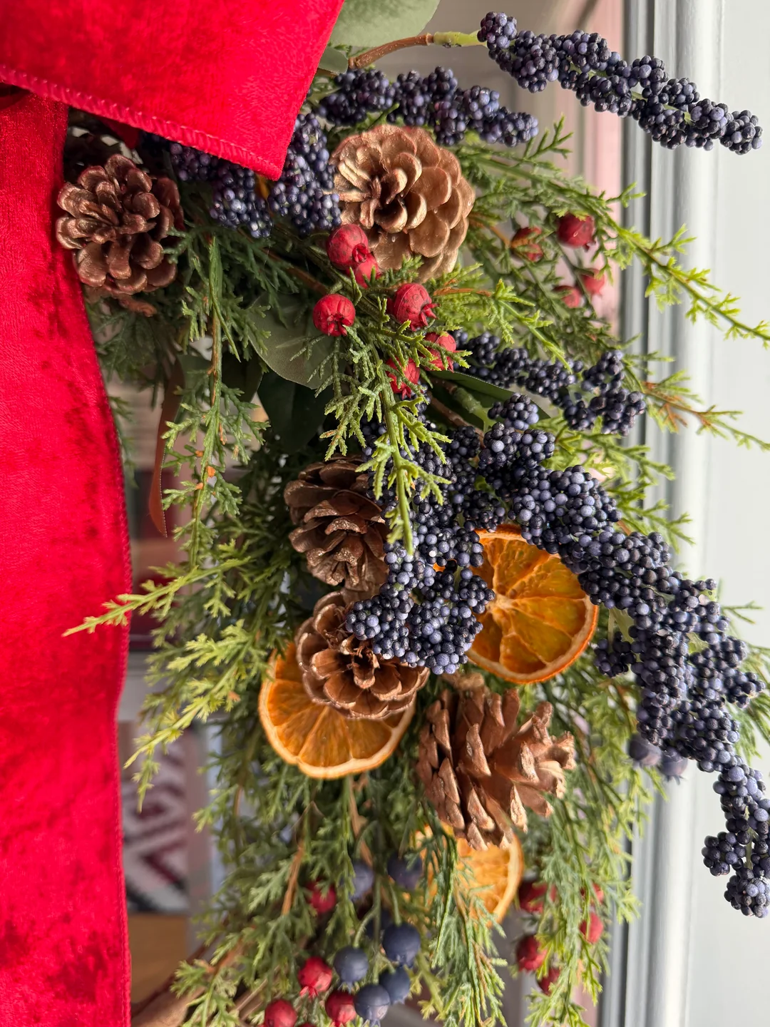 Close-up of evergreen foliage, red bow, pinecones, berries, and dried orange slices