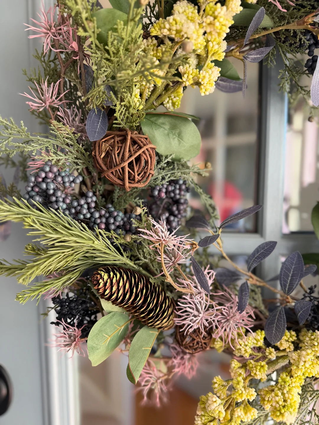 Close-up of greenery, yellow and purple accents, pinecones, and dark berries